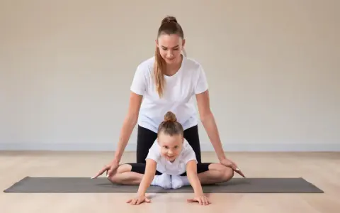 Frau und Kind machen Yoga. Das Kind krabbelt auf der Matte, die Frau unterstützt es. Yoga mit Kindern unter 3 Jahren fördert spielerisch die Bewegung.
