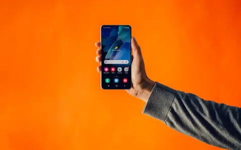 En hand håller upp en smartphone mot en orange bakgrund. Kanske en lösning på problem med dubbla simkort?