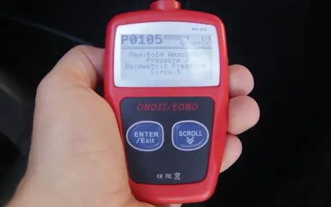 Ręka trzyma czytnik OBD, wyświetlający kod błędu P0105: "Manifold Absolute Pressure / Barometric Pressure Circuit". To jeden z wielu kodów błędów OBD po polsku.