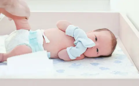 Noworodek z niezagojonym pępkiem leży na przewijaku. Dłoń rodzica podtrzymuje nóżkę dziecka.
