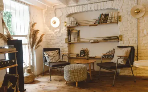 Acogedor rincón de lectura con sillas cómodas, mesa auxiliar, estanterías llenas de libros y plantas secas.