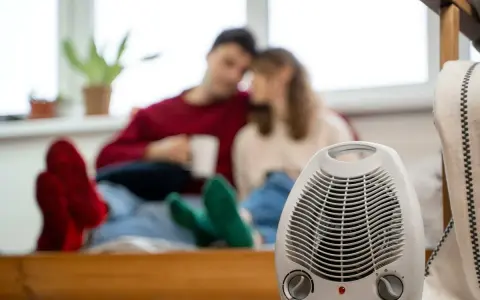 Pareja acurrucada con bebidas calientes, un radiador eléctrico en primer plano. Así funciona un radiador eléctrico para calentar el hogar.