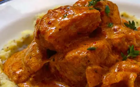 Sabroso pavo en salsa cremosa, adornado con hierbas frescas, servido sobre puré de patatas.