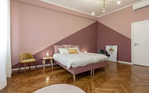 Camera da letto con pareti bicolore, un letto rosa, una sedia gialla e un parquet a spina di pesce. Un esempio di come pitturare una stanza con stile.