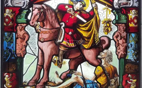 Święty Gracja na koniu przecina płaszcz dla żebraka. Witraż pełen symboli i postaci.