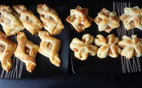 Pyszne przekąski z ciasta francuskiego z jabłkami, posypane cukrem, prezentują się apetycznie na czarnych talerzach.