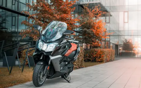 Elegancki skuter BMW C 650 GT z brązową kanapą stoi przed nowoczesnym budynkiem, otoczony jesienną zielenią.