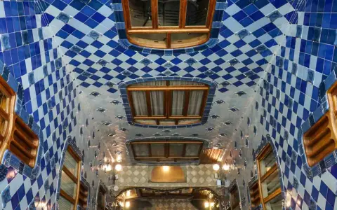Interno della Casa Batlló: soffitto ondulato con piastrelle blu e bianche a rombi, finestre in legno e luci soffuse.
