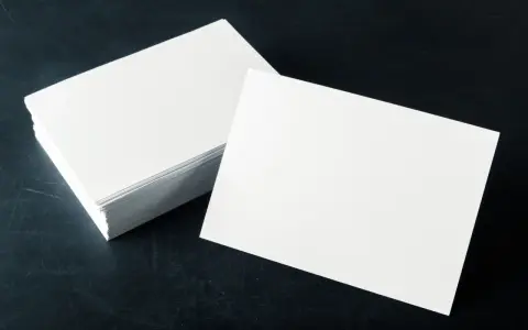 Pila de tarjetas blancas sobre fondo oscuro. El gramaje del papel es ideal para impresiones de alta calidad.