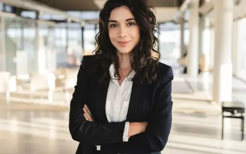 Kobieta w marynarce i białej koszuli, idealnie wpisująca się w **business casual dress code**, pewnie patrzy w obiektyw.