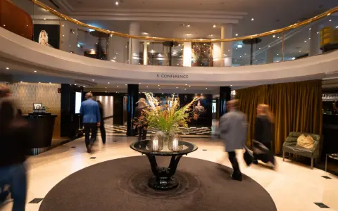 Elegant hotell park lobby med en blomsterdekor i mitten. Människor rör sig förbi i en suddig rörelse.