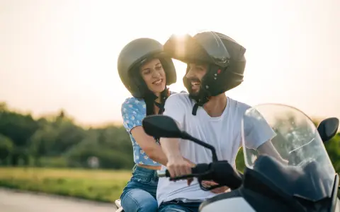 Pareja feliz en moto, disfrutando del atardecer. El sol brilla sobre sus cascos, creando un ambiente de aventura y libertad. CSRNET A2.