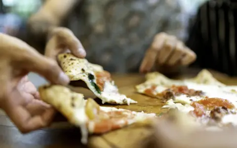 Hände greifen nach dampfenden Pizzastücken. So wie essen Italiener Pizza: gemeinsam, genussvoll, mit Freunden.