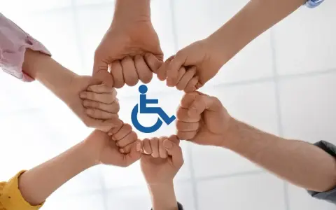 Dłonie tworzą krąg wokół symbolu niepełnosprawności, symbolizując wsparcie i integrację.