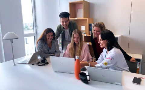 Zespół młodych ludzi pracuje razem przy biurku w biurze Alstom Wrocław, śmiejąc się i patrząc na ekran laptopa.