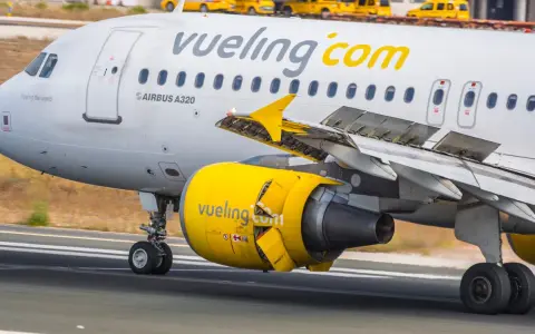 Samolot linii Vueling, hiszpańskie linie lotnicze, z żółtym silnikiem i logo na skrzydle, kołuje po pasie startowym.