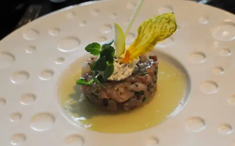 Un tartare de poisson finement préparé, garni de crème, herbes fraîches et d'une fleur jaune, une des spécialités Limoges.