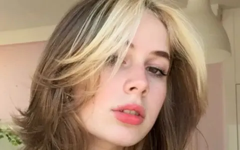 Dziewczyna z burzą blond i brązowych włosów w stylu curly wolf cut, z pasemkami przy twarzy.
