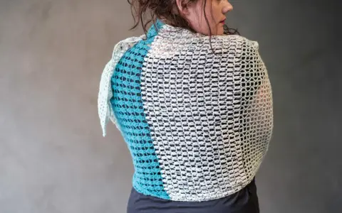 Mujer de espaldas con un cubre hombros a crochet de dos colores, blanco y azul turquesa, con un diseño calado.