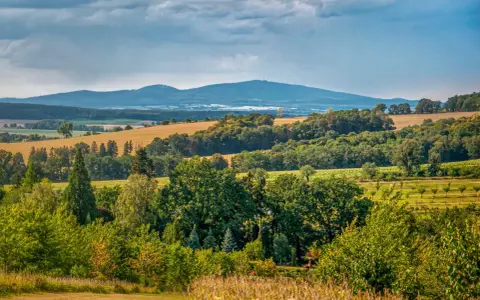 Malowniczy krajobraz z pagórkami i lasami, typowy dla **Gór Dolnośląskich**. W oddali widać pasmo górskie pod zachmurzonym niebem.