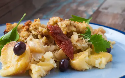 Morue à bras, un plat réconfortant avec des flocons de poisson, des olives noires, des tomates séchées et une touche de persil frais.