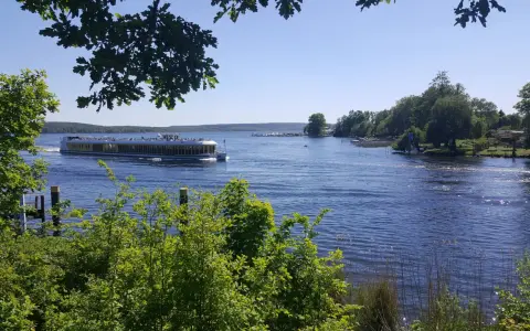 Ein Ausflugsboot fährt auf einem glitzernden See bei Potsdam. Grüne Bäume säumen das Ufer, ideal für einen entspannten Tag an den Badeseen Potsdam.