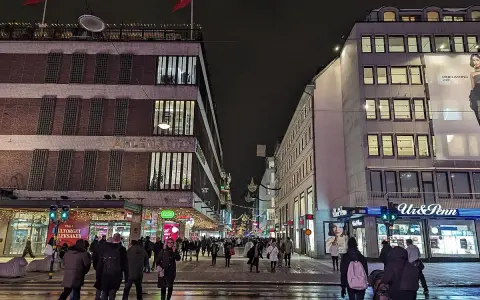 En livlig stockholm shopping street på kvällen. Folk promenerar förbi Åhléns City och Ur & Penn.