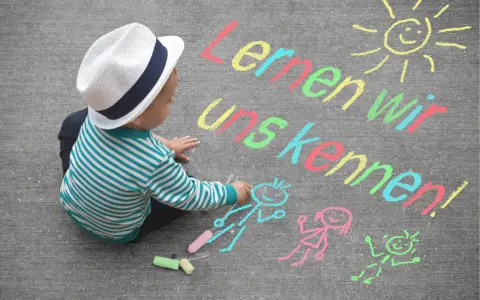 Kleiner Junge mit Hut malt mit Kreide auf Asphalt. Namensspiele für Kinder: "Lernen wir uns kennen!" mit Sonne und Figuren.