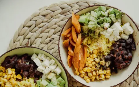 Zwei Schüsseln mit gesunden Reis Rezepten zum Abnehmen: Reis, Bohnen, Mais, Süßkartoffeln, Avocado und Feta.