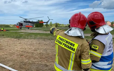 Strażacy w akcji. W tle lądujący śmigłowiec, który wspiera pracę w straży pożarnej.