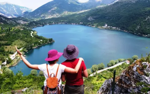 Coppia ammira un lago a forma di cuore, circondato da montagne verdi e alberi.