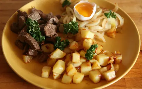 En tallrik med stekt kött, stekt potatis, stekt lök och ett kokt ägg. En klassisk rätt som representerar svenskt mat.