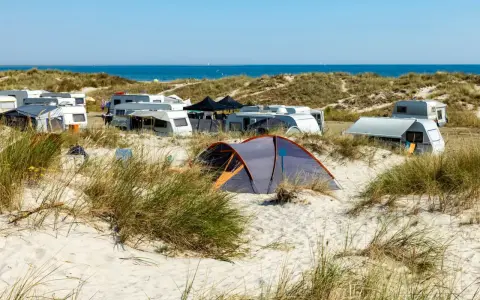 Ein sonniger Campingplatz in Deutschland am Meer. Wohnwagen und Zelte stehen zwischen Dünen und Strandhafer.