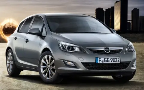 Szary Opel Astra J 1.7 CDTI z nowoczesnymi światłami i felgami, na tle miasta i energetycznego kręgu.