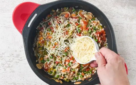 Un delicioso risotto de verduras en una sartén, con queso rallado a punto de ser añadido.
