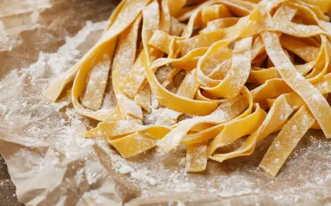 Świeży, domowy makaron tagliatelle, posypany mąką, czeka na gotowanie. Idealny przepis, jak zrobić makaron.