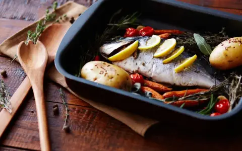 Pescado al horno con patatas, zanahorias y tomates, listo para servir.