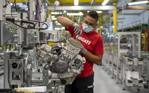 Operaio con mascherina e guanti lavora su un motore Ducati in fabbrica. Un'emozione da museo.