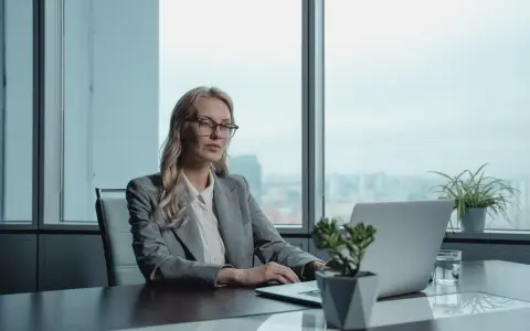 Kobieta w okularach pracuje przy laptopie, przygotowując list motywacyjny na stanowisko kierownicze. Wzór dokumentu jest kluczowy.