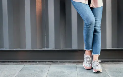 Nogawki jeansów postrzępione na dole, w połączeniu z błyszczącymi sneakersami, tworzą modny look.