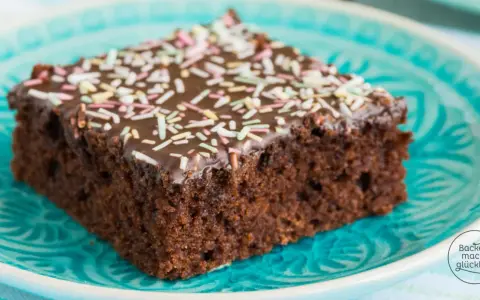 Ein Stück saftiger Schokoladen-Blechkuchen mit Schokoladenglasur und bunten Streuseln auf einem türkisfarbenen Teller. Ein einfaches Blechkuchen Rezept für Glücksmomente.