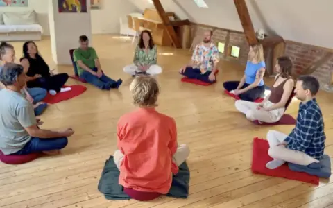 Menschen sitzen im Kreis auf Meditationskissen. Eine Gruppe genießt eine **Auszeit im Kloster**, umgeben von Ruhe und Gemeinschaft.