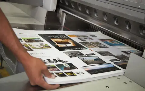 Mani che sistemano fogli stampati su una macchina da taglio, parte della post produzione di una rivista.