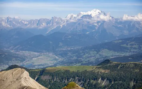 Vue panoramique des Alpes, avec le Mont Blanc enneigé, point culminant des Alpes, dominant la vallée verdoyante et ses villages.