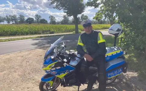 Policjant w pełnym umundurowaniu siedzi na swoim policyjnym motocyklu, gotowy do służby.