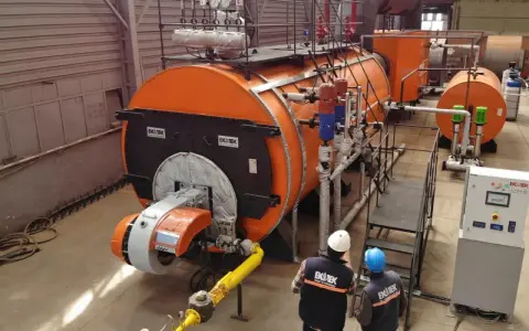 Dos técnicos observan varios tipos de calderas industriales naranjas y grises en una fábrica.