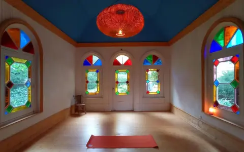 Un tapis de yoga orange attend dans une pièce lumineuse aux vitraux colorés, créant une atmosphère de maison bienveillante.
