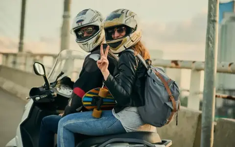 Para z kaskami na skuterze, dziewczyna pokazuje znak pokoju. Czy z prawem jazdy AM można wozić pasażera?