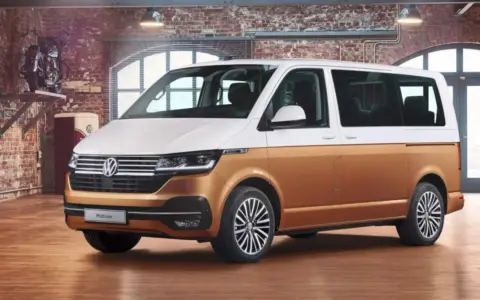 Biało-złoty bus osobowy Volkswagen Multivan w garażu z ceglaną ścianą.