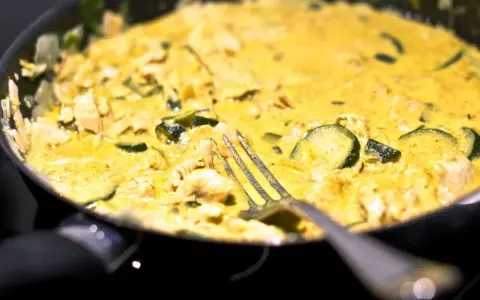 Pyszne curry z cukinią i kurczakiem w kremowym sosie, gotowe do podania. Widelec czeka na pierwszy kęs.
